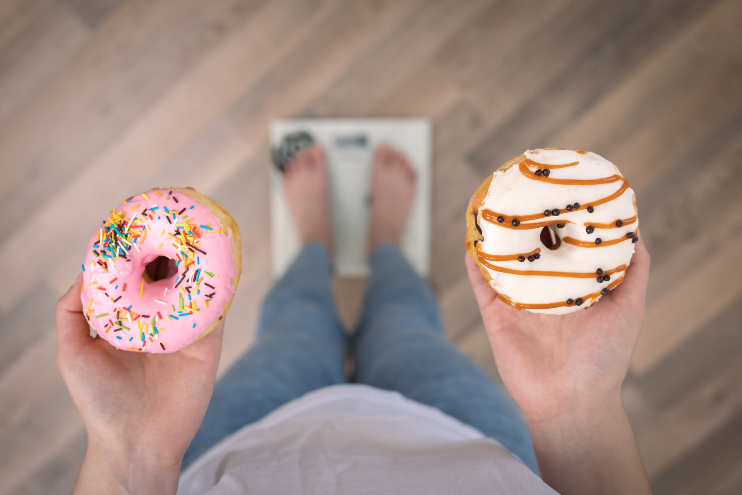 A woman stands on the scales, holds donuts in her hands, top view, copy space.